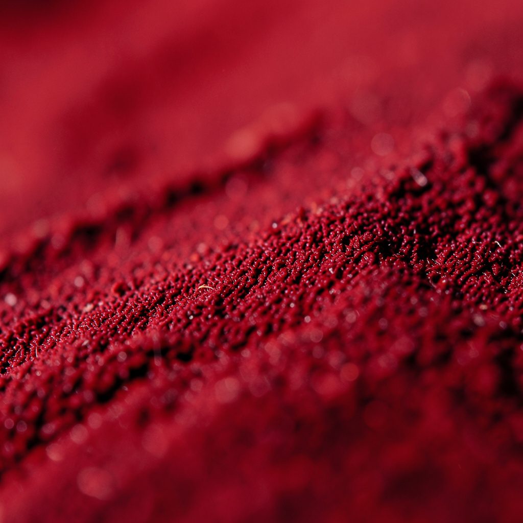 Extreme close-up photograph of a rough beige paper texture with soft fibres, warm light and subtle shadows, evoking a printed magazine feel.