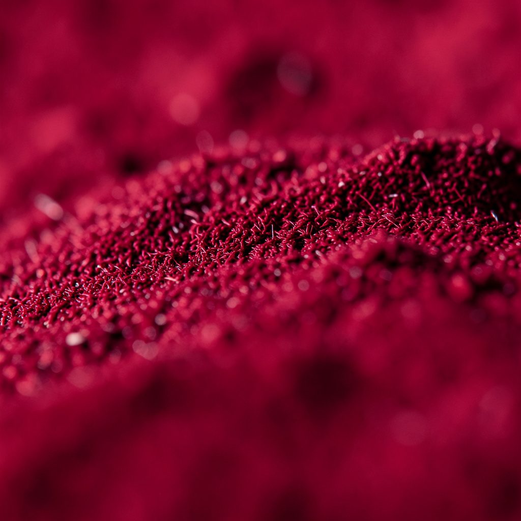 Extreme close-up photograph of crushed rose-pink and coral cosmetic powder forming a soft, matte texture across the frame, warm and feminine mood.